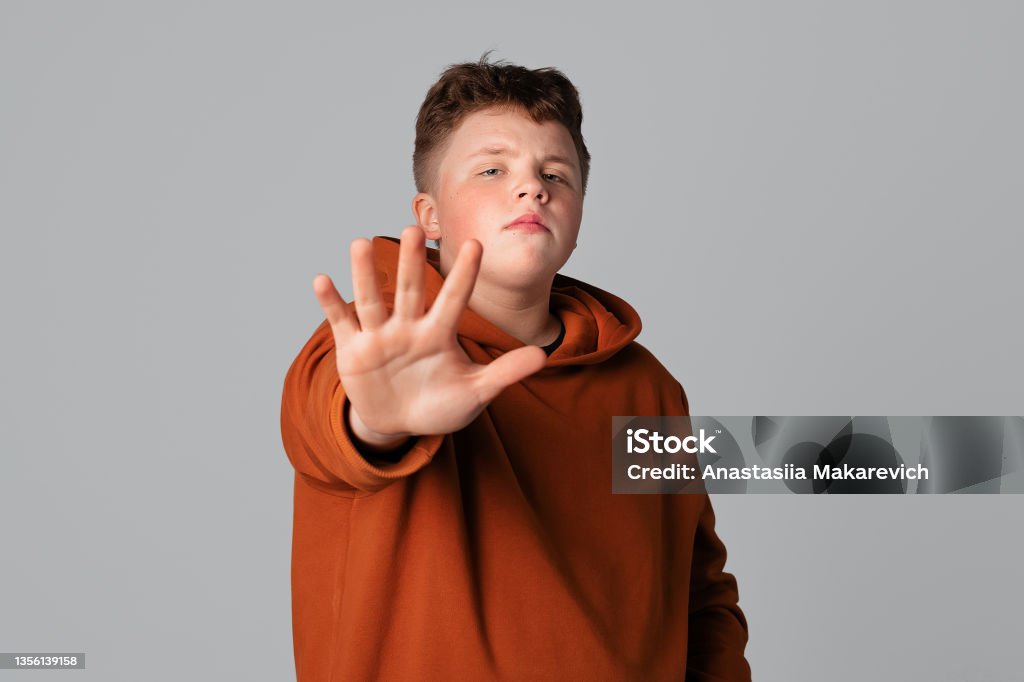 Confident serious teenager boy showing stop sign, lifting open palm and saying No Confident serious teenager boy showing stop sign, lifting open palm and saying No. Guy making refusal warning gesture with hand in front of him, expressing refusal 16-17 Years Stock Photo