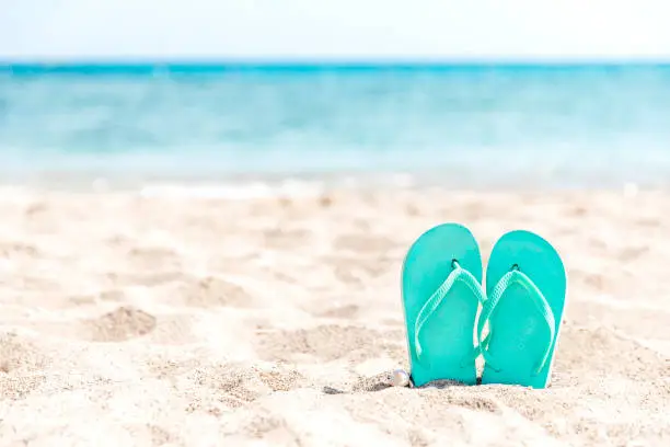 Turquoise or light blue flip flops or sandal shoe stuck in the sand on sandy beach by the sea coastline or ocean. Travel or vacation concept in hot countries in summer or winter. High quality photo