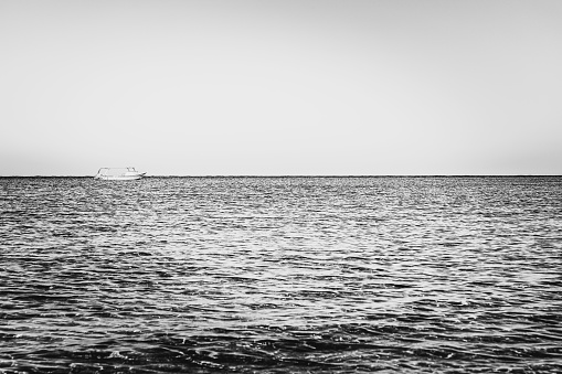 Black-white vessel, yacht photography. Alone white boat, ship in silent sea or ocean water surface. A quiet and peaceful harbor bay. Waves tranquil mood. Transportation business. Blurred background