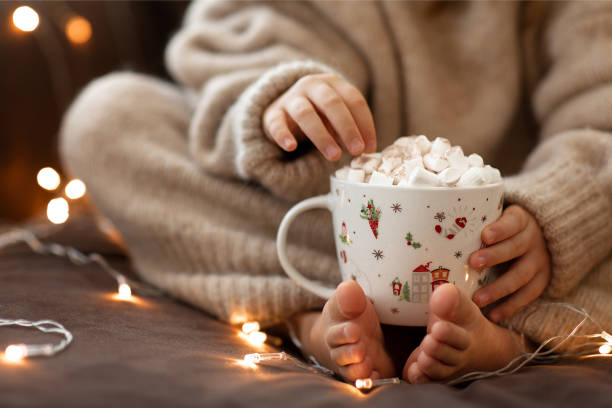 아이 맨발과 손은 뜨거운 코코아 마시멜로 가깝고 화환 조명을 닫습니다.flaffy 퍼지 퍼지 따뜻한 니트 베이지 스웨터. 크리스마스 컨셉, 휴일. 새해 복 많이 받으시면 새해.소파 집에 앉아 있는 � - baby cup 뉴스 사진 이미지
