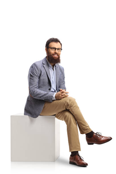 istock Bearded man sitting on a white cube and smiling 1356140504