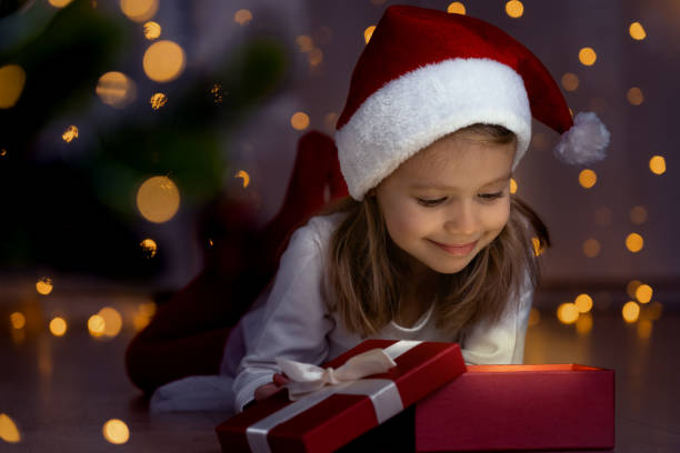 istock Girl at dark opens box with magic light next to christmas tree. New Year gift 1356140550