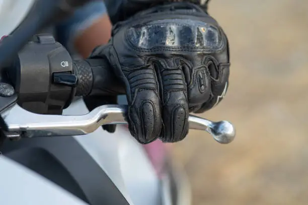 detail of the left hand of a biker with a black leather glove on the clutch lever of his motorcycle