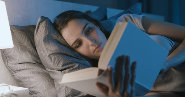 Woman lying in bed and reading a book stock photo