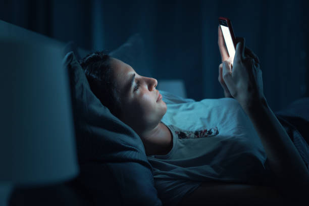 Young woman lying in bed and using her smartphone stock photo