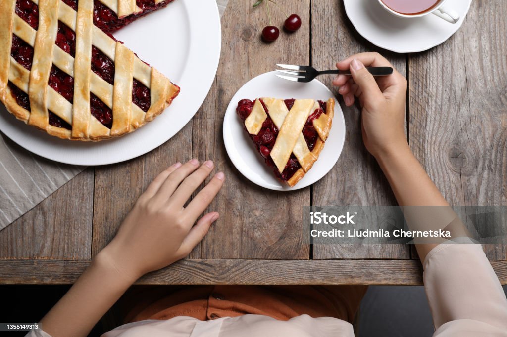 Woman eating delicious cherry pie at wooden table, top view Eating Stock Photo
