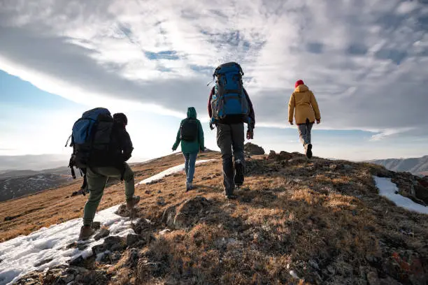 Group of four diverse tourists or hikers are walking on mountain top at sunset time