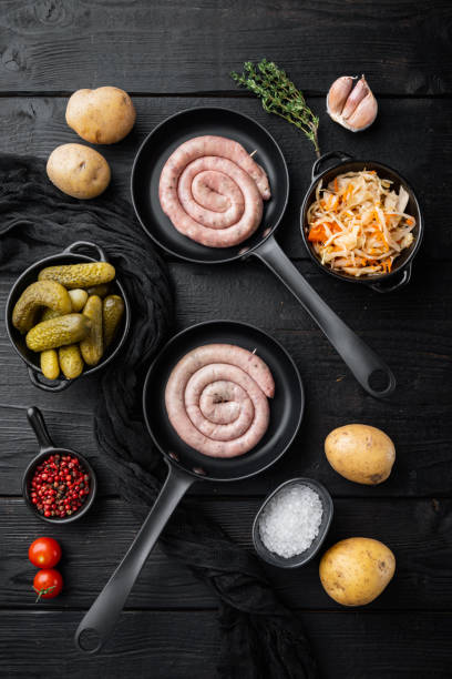 salsichas alemãs tradicionais com purê de batatas e chucrute em frigideira de ferro fundido, no fundo da mesa de madeira preta, vista superior plana lay - german culture salad prepared potato bratwurst - fotografias e filmes do acervo