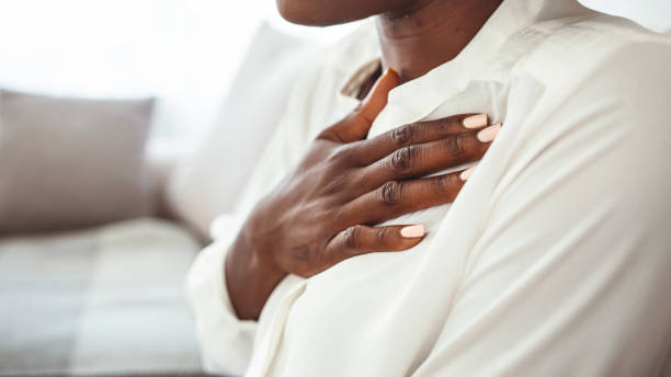 girl having respiration problems touching chest sitting on a couch in the living room at home. - women sadness african ethnicity african descent imagens e fotografias de stock