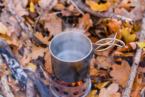 top view of a metal mug with boiling water on an open fire in the autumn forest