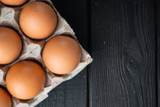 istock Chicken eggs in an egg box tray, on black wooden table background, top view flat lay , with space for text  copyspace 1356154610