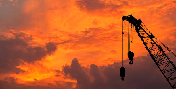 Close-up silhouette industrial big crane with steel hook for work on construction building outdoor site on sunset sky