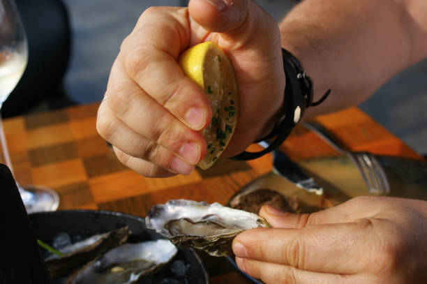 istock fresh oysters. hand squeezes lemon juice into fresh oyster 1356157037