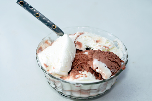Selective focus of vanilla and chocolate ice cream scoops in a glass bowl with a teaspoon isolated and ready to be served isolated, mixed vanilla and chocolate ice cream