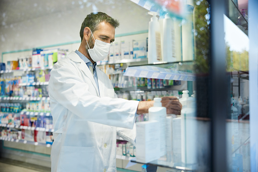 Waist-up view of a pharmacist, he is arranging medicines on the shelves.