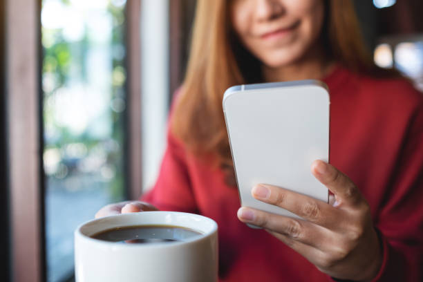 istock a young woman holding and using mobile phone while drinking coffee in cafe 1356159910