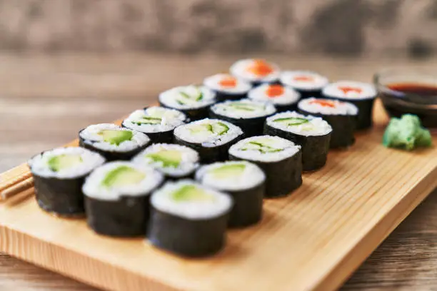 Wooden board with avocado, salmon and cucumber sushi makis on a wooden surface