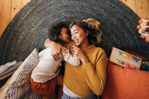 Overhead view of a mother and her daughter lying on the floor Overhead view of a mother and her daughter lying on the floor in their play area. Affectionate mother smiling happily while embracing her daughter. Mother and daughter spending quality time at home. young family stock pictures, royalty-free photos & images