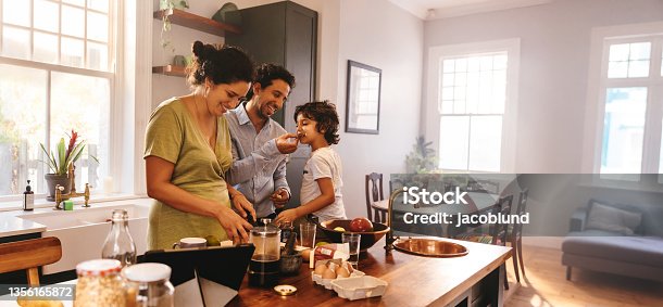 istock Playful dad feeding his son a slice of bread in the kitchen 1356165872