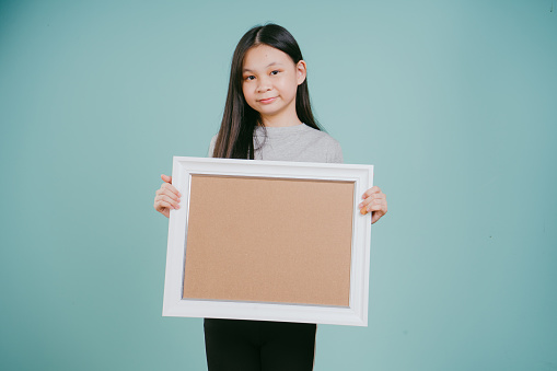 An Asian Chinese girl holding a blank frame isolated on a green background.