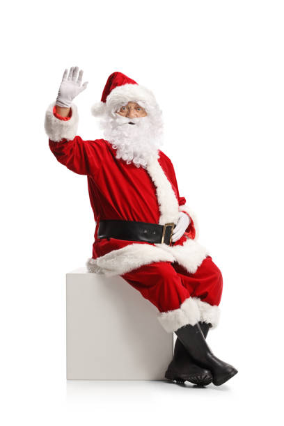 Santa claus sitting on a white cube and waving at camera