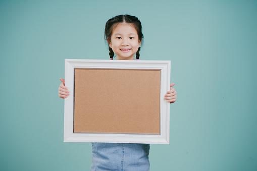 An Asian Chinese girl holding a blank frame isolated on a green background.