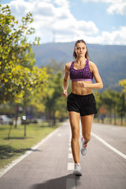 Female wearing crop top and shorts and running towards camera outdoors Female wearing crop top and shorts and running towards camera outdoors on a running lane running shorts stock pictures, royalty-free photos & images