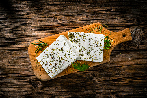 Regional food backgrounds: Overhead view of two blocks of Greek feta cheese on a cutting board shot on rustic wooden table. High resolution 42Mp studio digital capture taken with SONY A7rII and Zeiss Batis 40mm F2.0 CF lens
