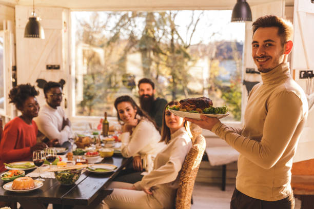 istock Man holding a dish and smiling at camera while serving to a group of friends 1356168285