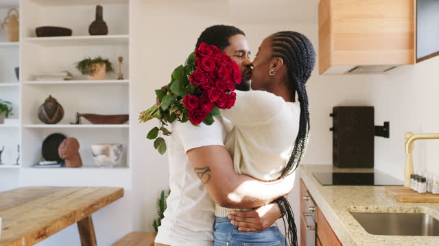 4k video footage of a handsome young man surprising his girlfriend with roses in the kitchen at home