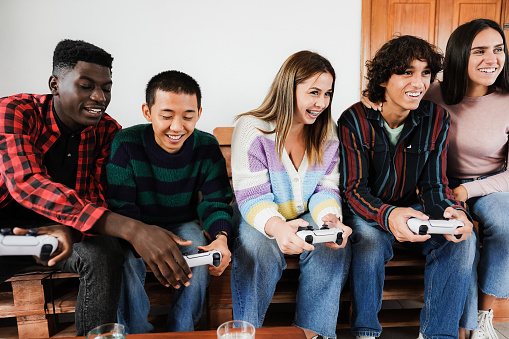 Multiracial young friends having fun playing video games at home - Focus on center girl face