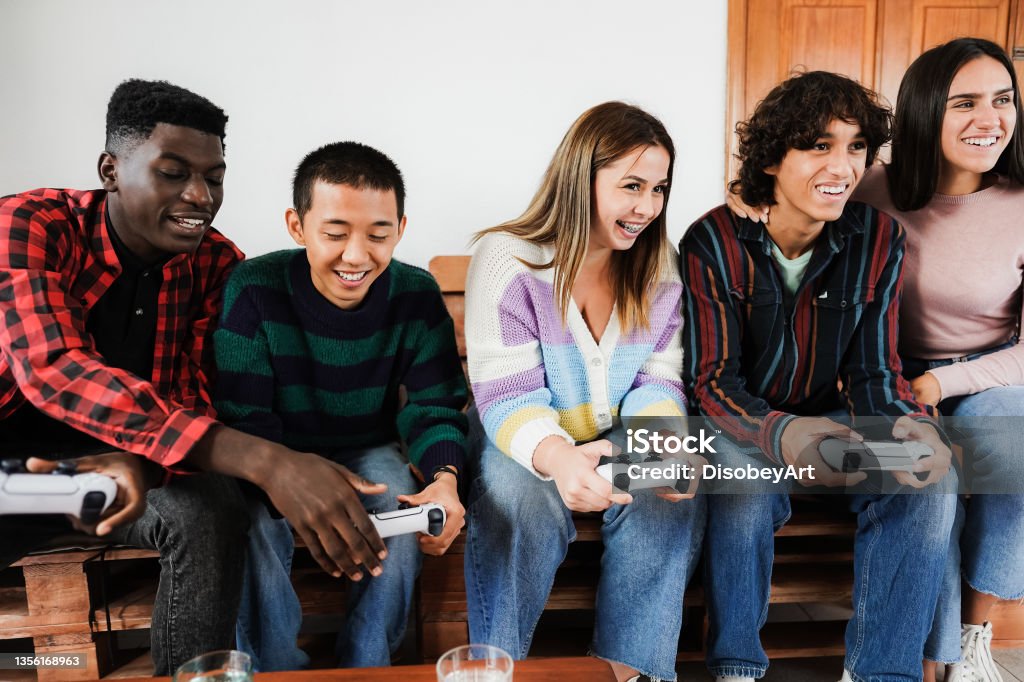 Multiracial young friends having fun playing video games at home - Focus on center girl face Video Game Stock Photo