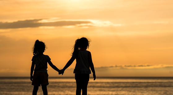 Little sisters holding hands at sunset near the beach
