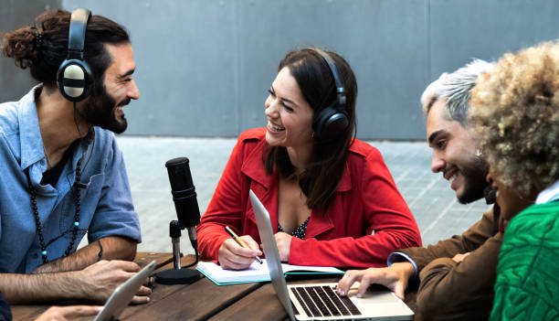 istock Smiling young influencers record podcast outdoors using microphone, headphones and laptop. Millennial content creators 1356171746