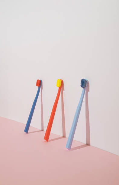 Trendy minimal composition with three colorful toothbrushes on pastel pink background. Modern aesthetic.