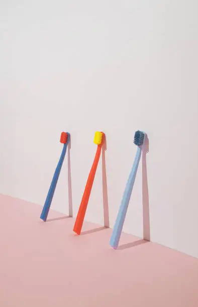 Trendy minimal composition with three colorful toothbrushes on pastel pink background. Modern aesthetic.