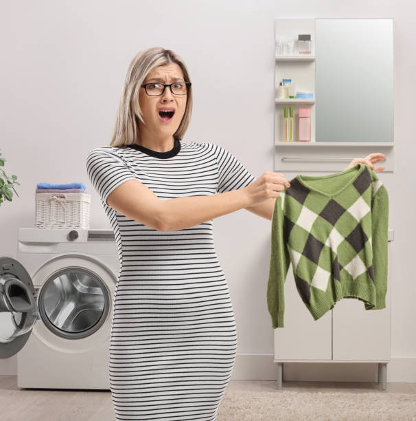 Angry young woman holding a shrunken blouse Angry young woman holding a shrunken blouse in a bathroom contracting stock pictures, royalty-free photos & images