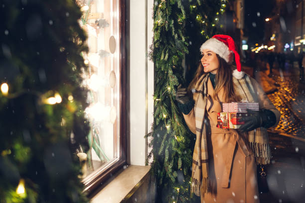 happy woman in santa's hat holding presents gift boxes by store showcase on city street at christmas season. - coat warm clothing one person joy imagens e fotografias de stock