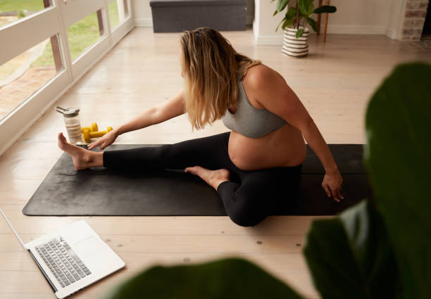 mujer caucásica embarazada que se estira en una esterilla de yoga mientras ve el video de entrenamiento - ewan fotografías e imágenes de stock