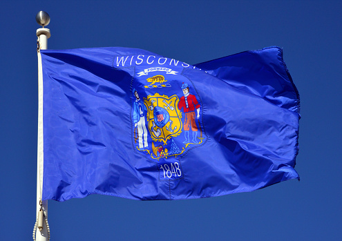 Milwaukee, Wisconsin, USA: Wisconsin state flag fluttering in the wind (real photo, not computer generated) - Shield on a dark blue field with the state motto \