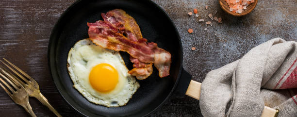 desayuno tradicional inglés con huevos fritos y tocino en sartén de hierro fundido sobre fondo de hormigón oscuro. vista superior. - photography metal traditional culture full fotografías e imágenes de stock