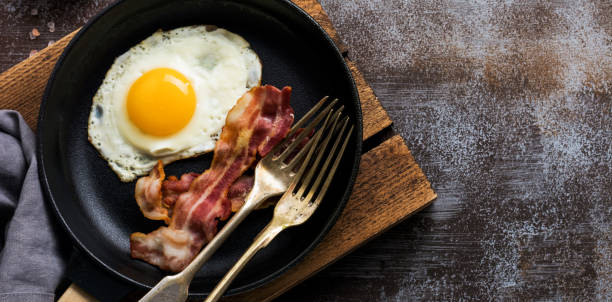 istock Traditional English breakfast with fried eggs and bacon in cast iron pan on dark concrete background. Top view. 1356186699