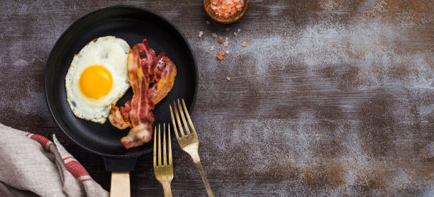 istock Traditional English breakfast with fried eggs and bacon in cast iron pan on dark concrete background. Top view. 1356186718