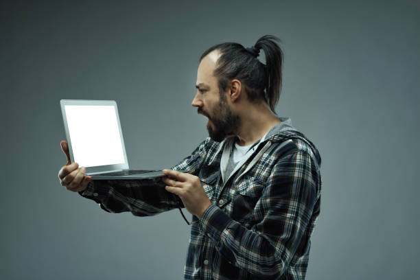Distraught man staring at his blank handheld laptop screen in horror and shock after receiving bad news leading to ongoing problems and adversity