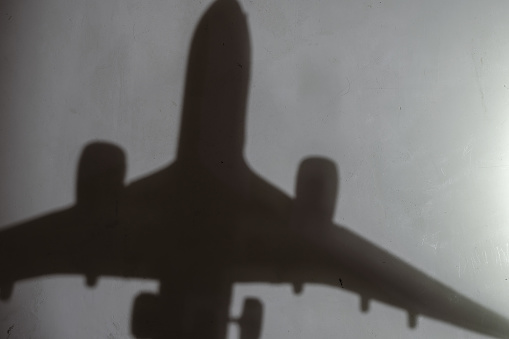 Blur, defocus, noise, grain effect. Dark silhouette of an airplane on a light gray wall. Indoor. Selective focus. No people.