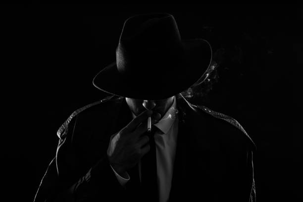 istock Old fashioned detective smoking cigarette on dark background, black and white effect 1356190782