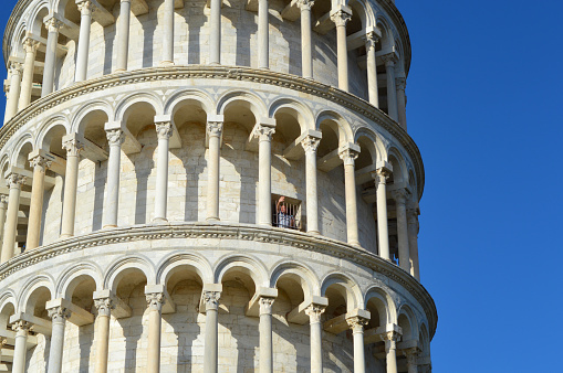 Pisa, Italy – 22nd October, 2021: One tourist waving from inside the world famous Leaning Tower of Pisa on a clear blue sky day.