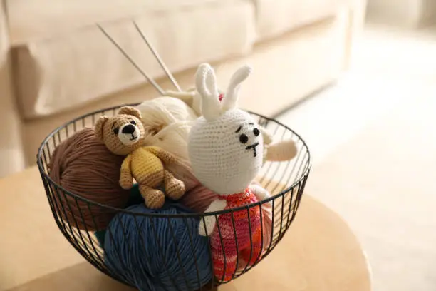 Basket with set of color threads and knitted toys on table indoors. Handicraft as hobby