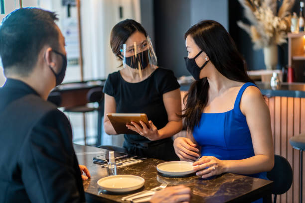 istock Asian waitress with face shield taking orders from customer at a restaurant. 1356192367