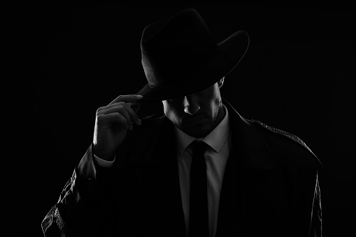 Old fashioned detective in hat on dark background, black and white effect